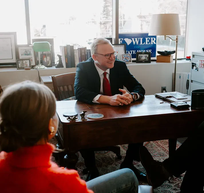 brann fowler shaking hand with a client across a desk in an office while a woman watches from a chair.