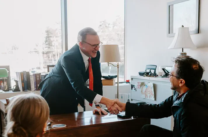 Brann Fowler shaking hand with a client across a desk in an office while a woman watches from a chair.