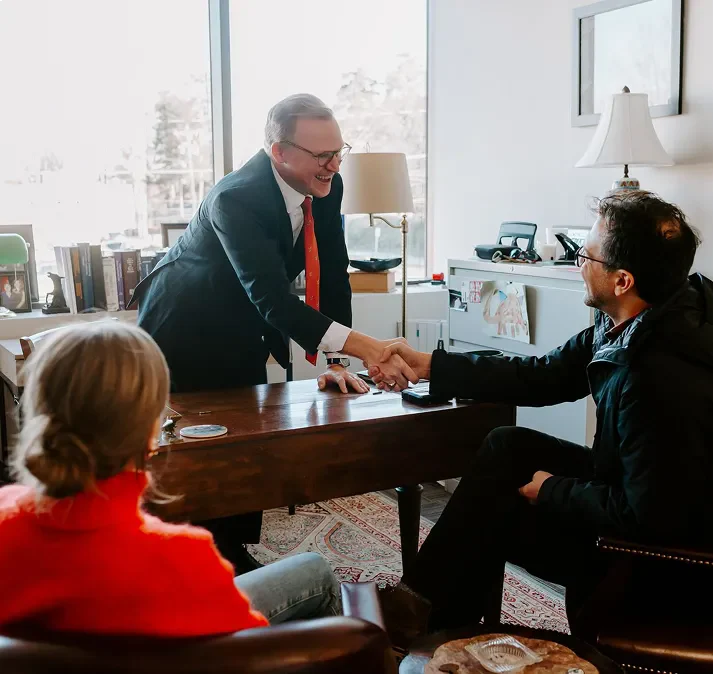 Brann Fowler shaking hand with a client across a desk in an office while a woman watches from a chair.